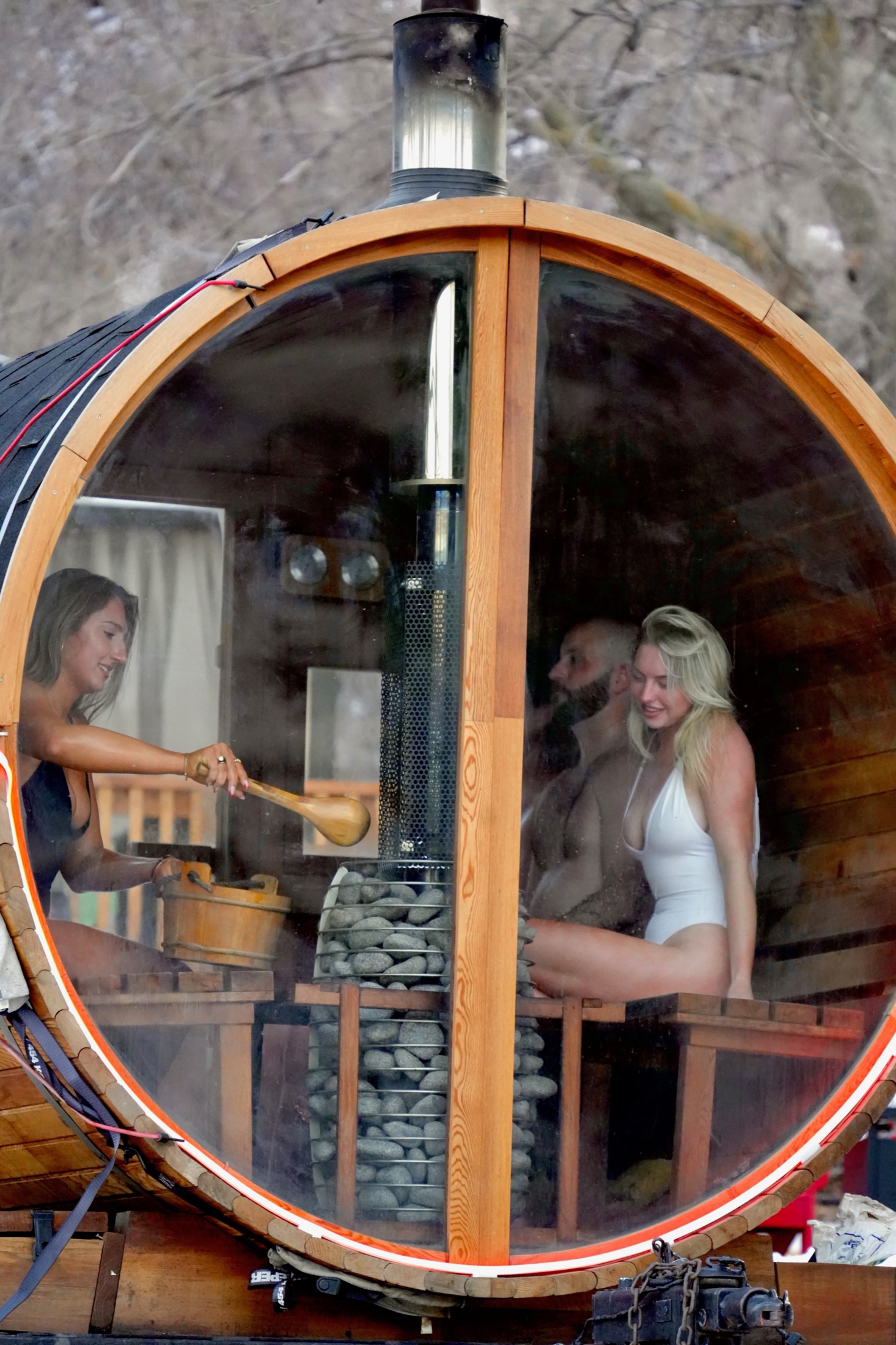 Four people inside a barrel sauna with wood-fired stove and a red rock view